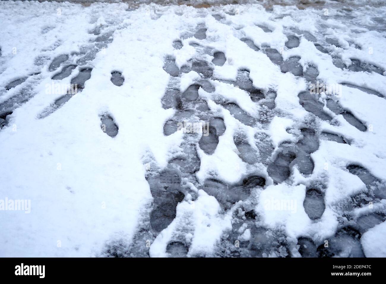 Street covered with snow and imprints of the shoes of the passers by. They disturb layer of snow that has not been cleared away. Stock Photo