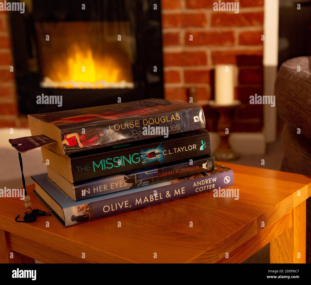 A pile of books on a coffee table in front of a real flame effect electric fire. Stock Photo