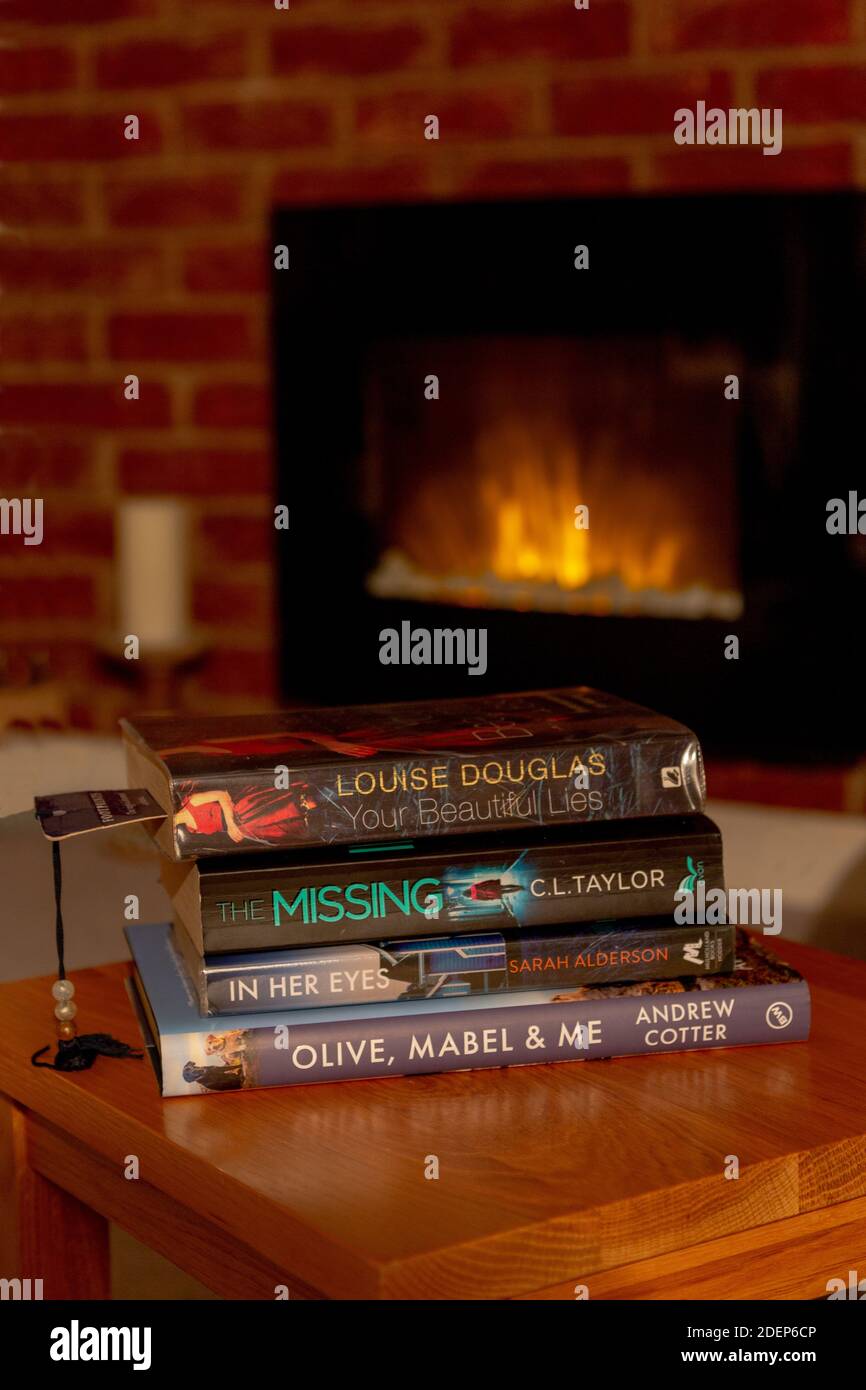 A pile of books on a coffee table in front of a real flame effect electric fire. Stock Photo