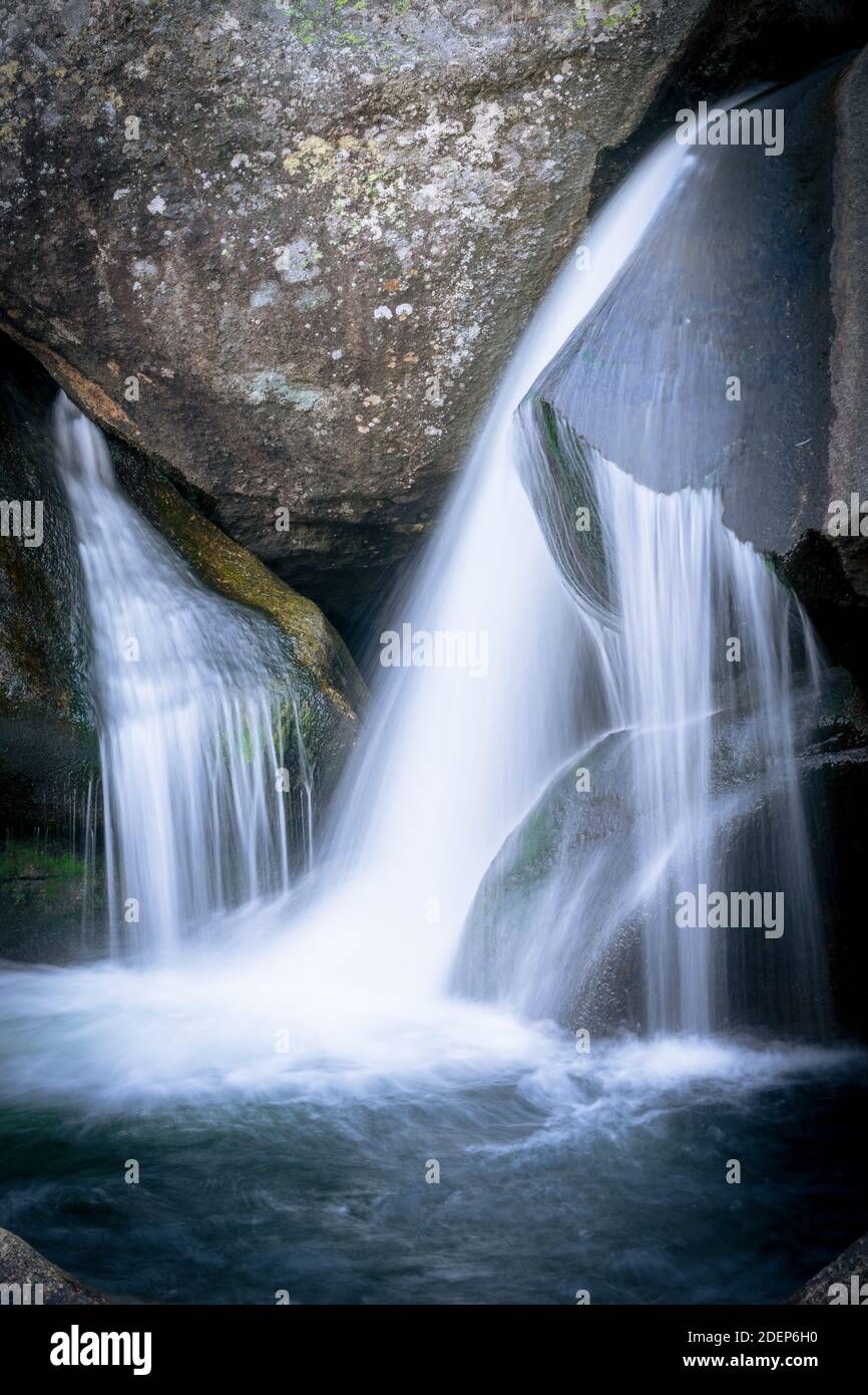 A vertical shot of a waterfall with long exposure surrounded by rocks ...