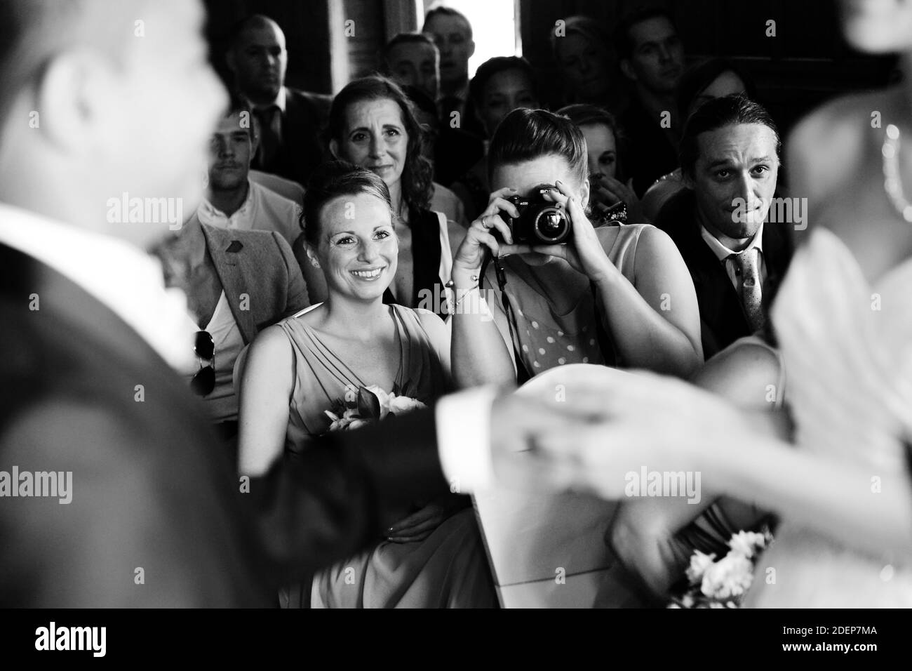 Seated wedding guest with compact SLR camera photographs wedding ceremony as bride and groom hold hands for their wedding vows Stock Photo