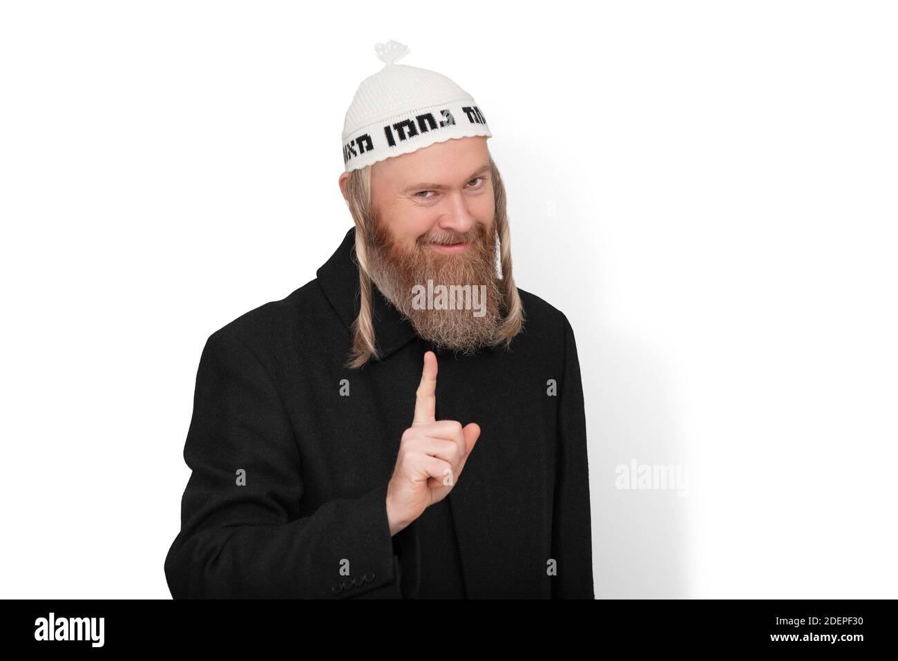 Smiling bearded jewish man with sidelocks in white kippah hinting do not try to deceive me. Charismatic sly jew dressed in black coat showing warning Stock Photo