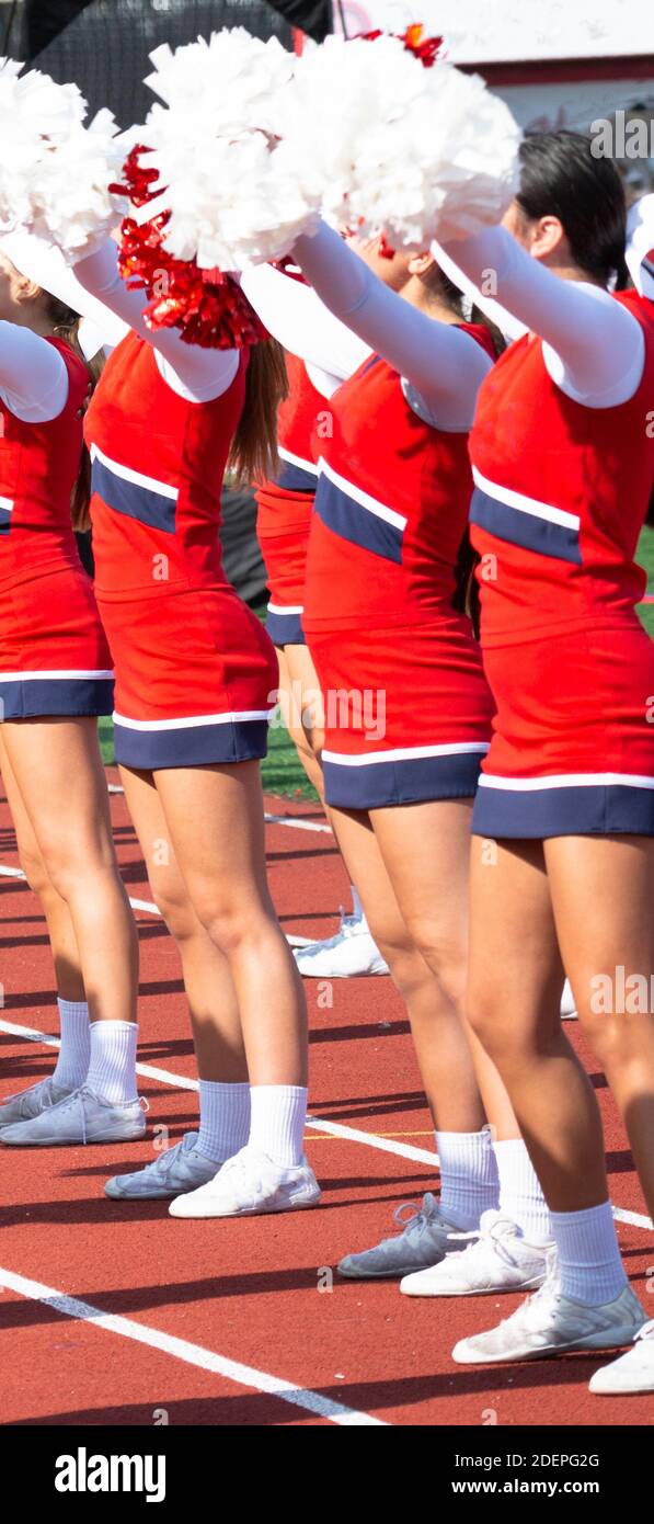 High School cheerleaders with their pompoms in the air while cheering to the fans during a football game. Stock Photo