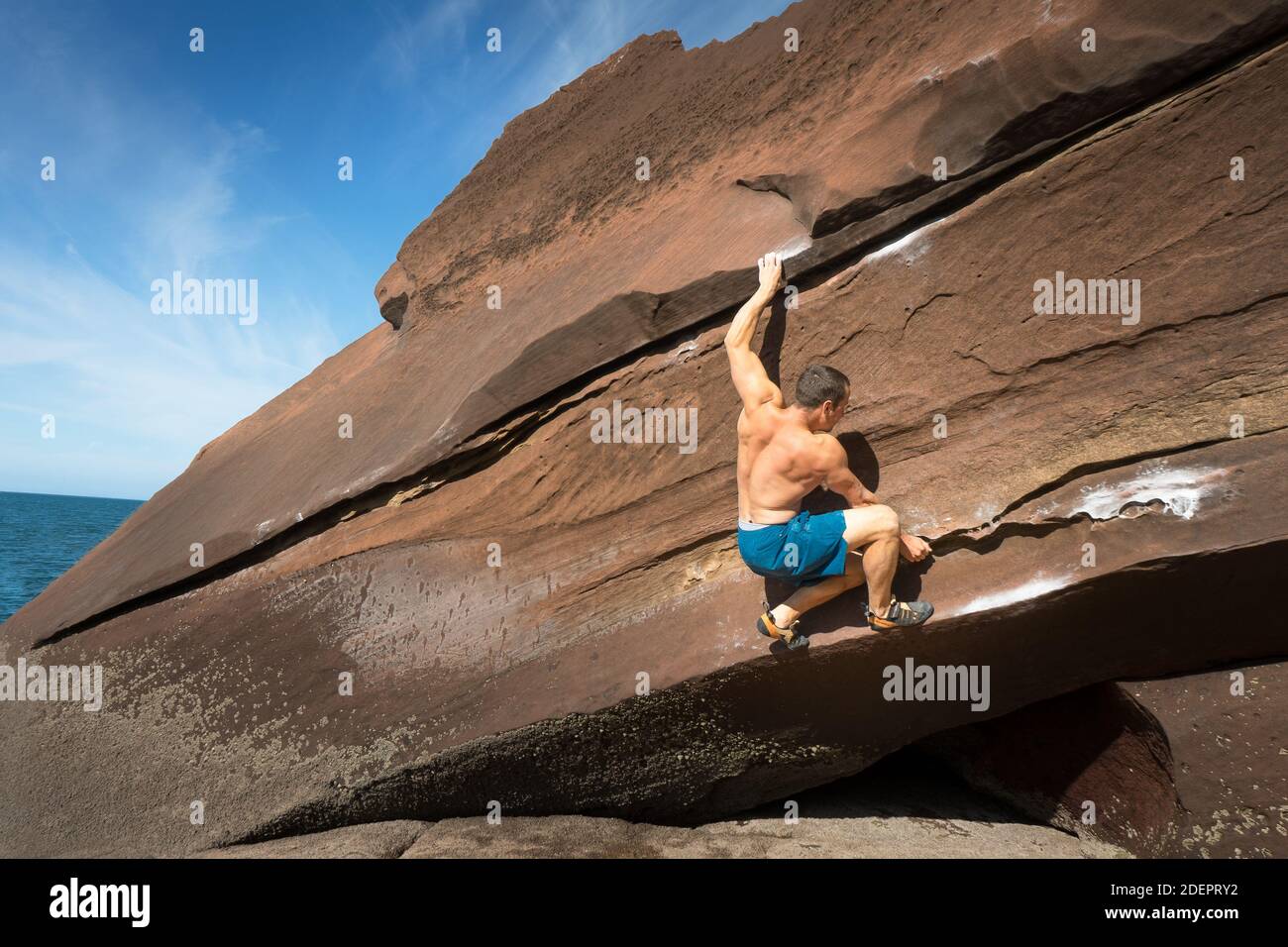 Man Climbing Hard Boulder Problem on a Sunny Day at St Bees, Cumbria, UK Stock Photo