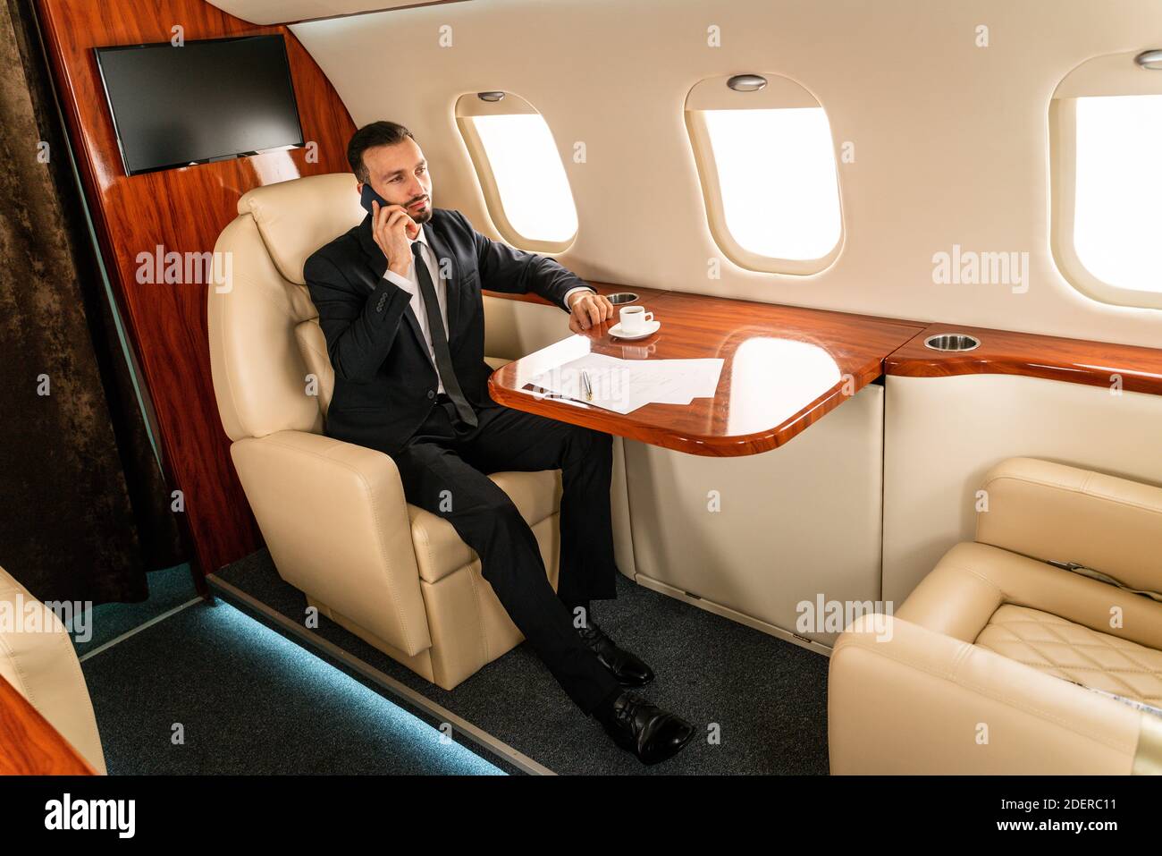 Handsome businessman wearing elegant suit  flying on exclusive private jet - Successful entrepreneur sitting in exclusive business class on airplane, Stock Photo