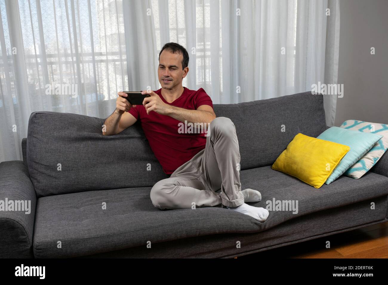 Mature man (44 years old) sitting on the couch and watching movie on his smartphone. Stock Photo