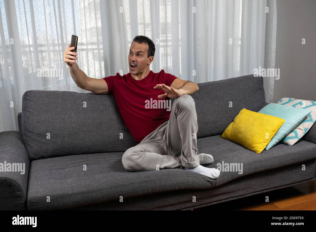 Mature man (44 years old) sitting on the couch and taking a picture of his grimace. Stock Photo
