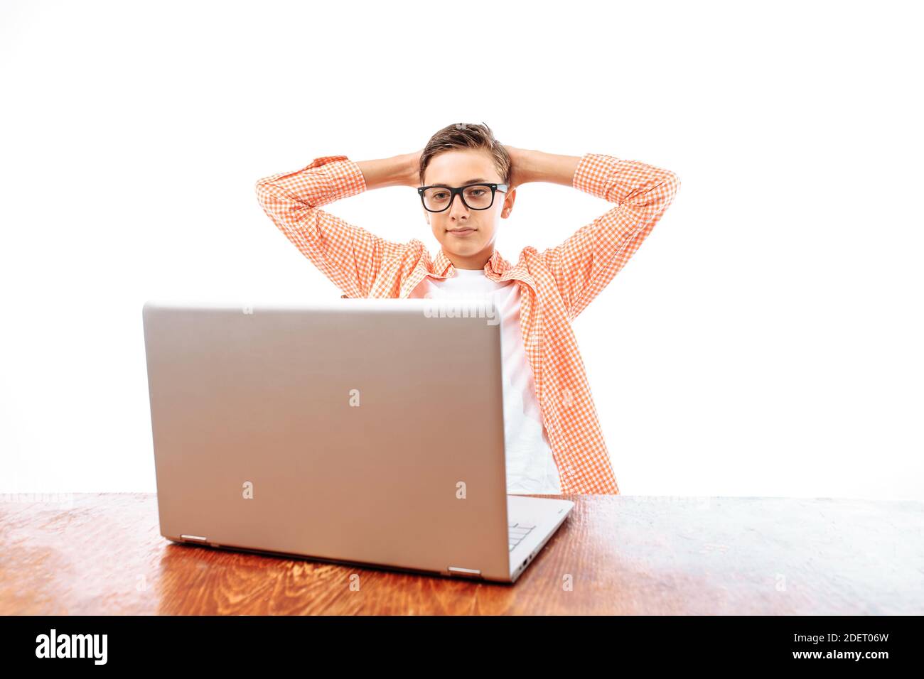 A young man resting after school sitting at the table and watching a movie on a laptop, throwing his hands behind his head, on a white background, in Stock Photo