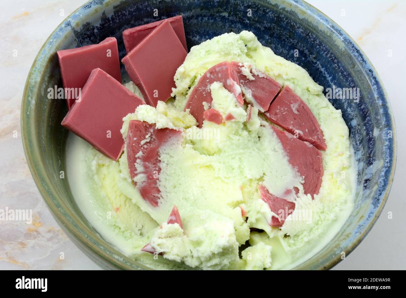 Layered pistachio sweet cream and ruby chocolate ice cream with ruby chocolate candy pieces on side in ceramic bowl on table Stock Photo