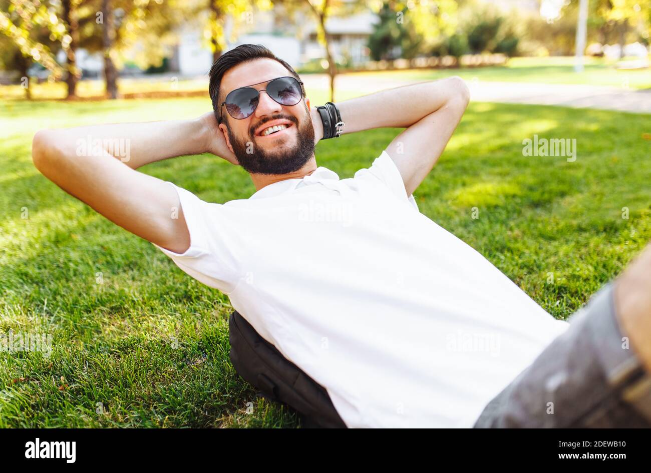 stylish hipster in white shirt, resting on the lawn in the Park, in a good mood Stock Photo