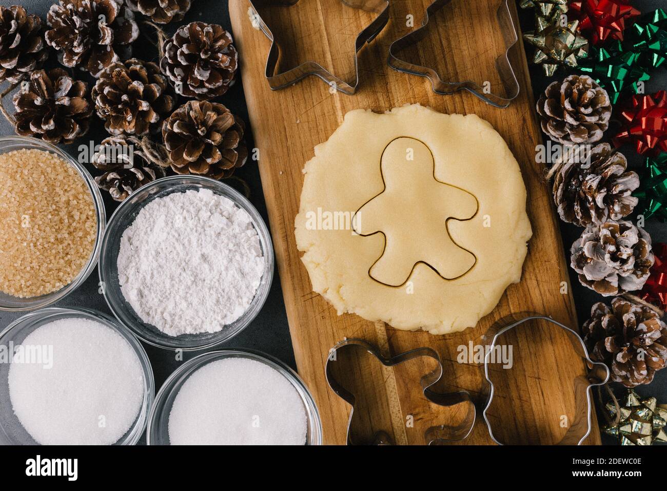 Christmas Ginger Bread Man Cookie Cutter In Raw Cookie Dough With Pine Cones, Holiday Ribbons, And Ingredients on Dark Slate Texture Stock Photo