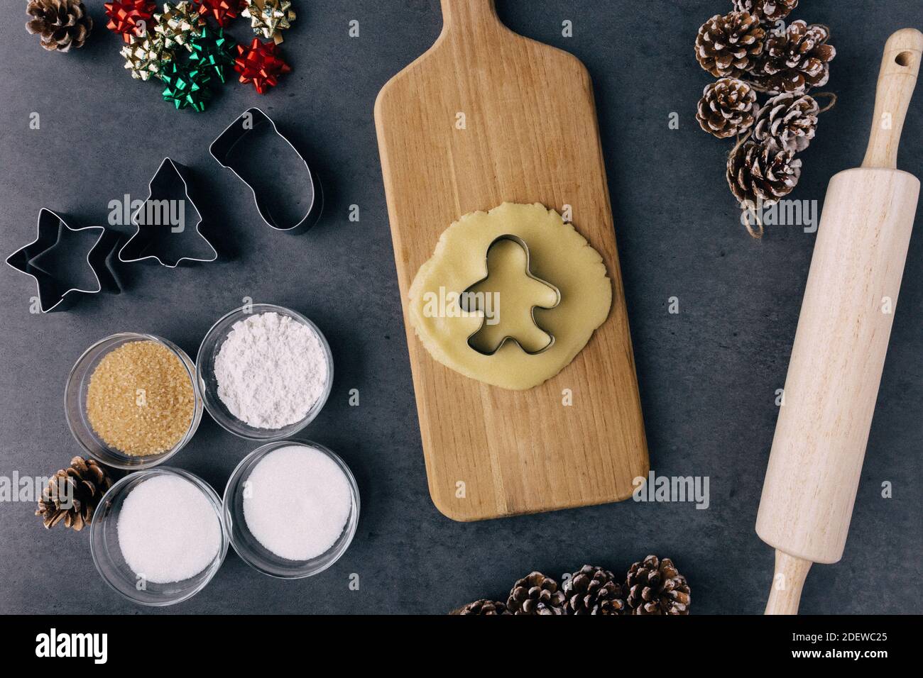 Christmas Ginger Bread Man Cookie Cutter In Raw Cookie Dough With Pine Cones, Holiday Ribbons, And Ingredients on Dark Slate Texture Stock Photo