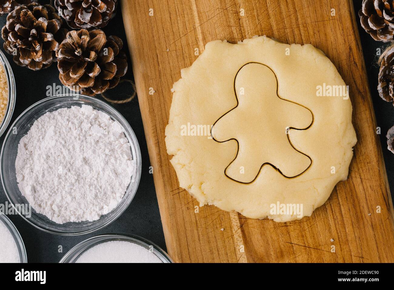 Christmas Ginger Bread Man Cookie Cutter In Raw Cookie Dough With Pine Cones, Holiday Ribbons, And Ingredients on Dark Slate Texture Stock Photo