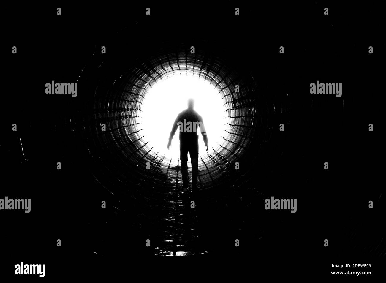 Silhouette of a man walking to the light at the end of a big tunnel ...
