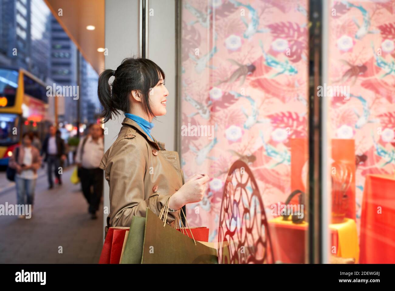 beautiful happy young asian woman shopper looking into shop window in modern city Stock Photo