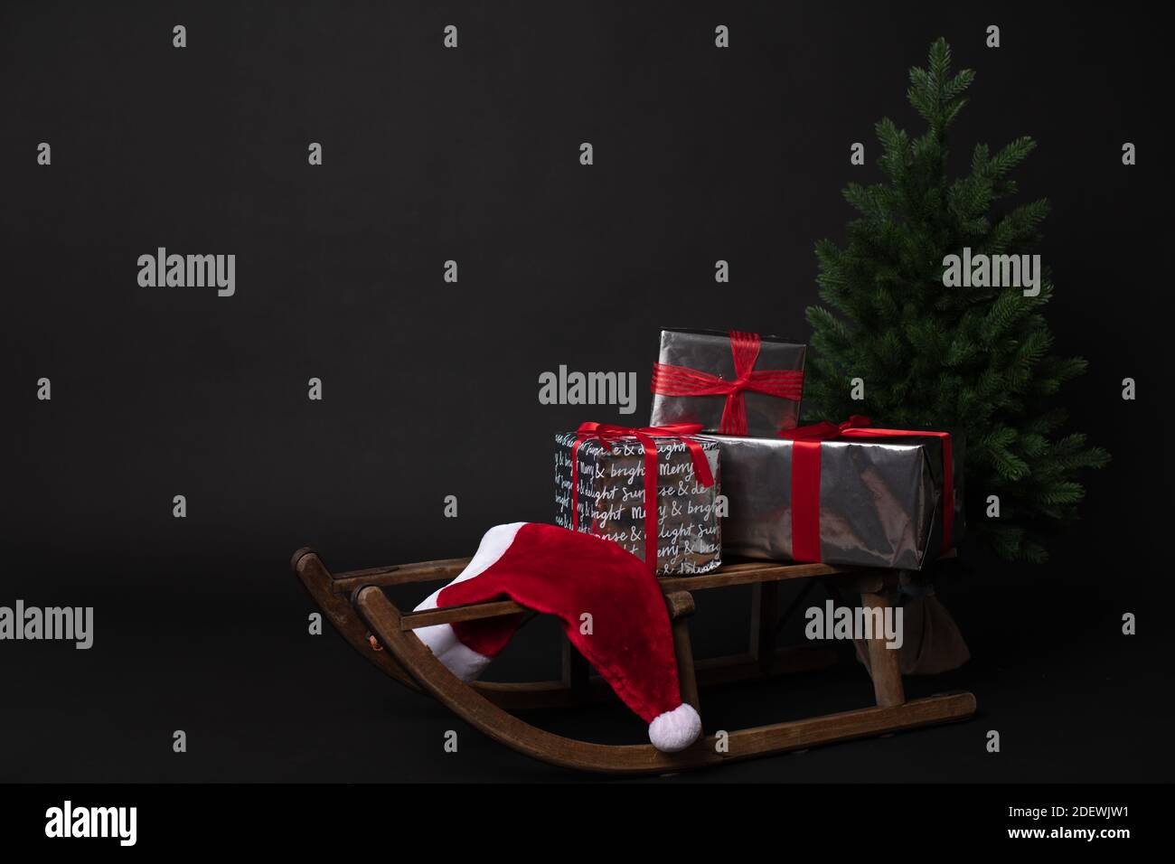 Rustic sleigh with gift boxes and Santas hat next to Christmas trees ...