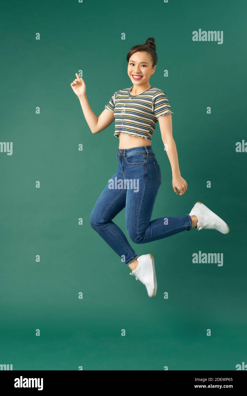 Full length photo of charming young woman in casual wear jumping over green background Stock Photo