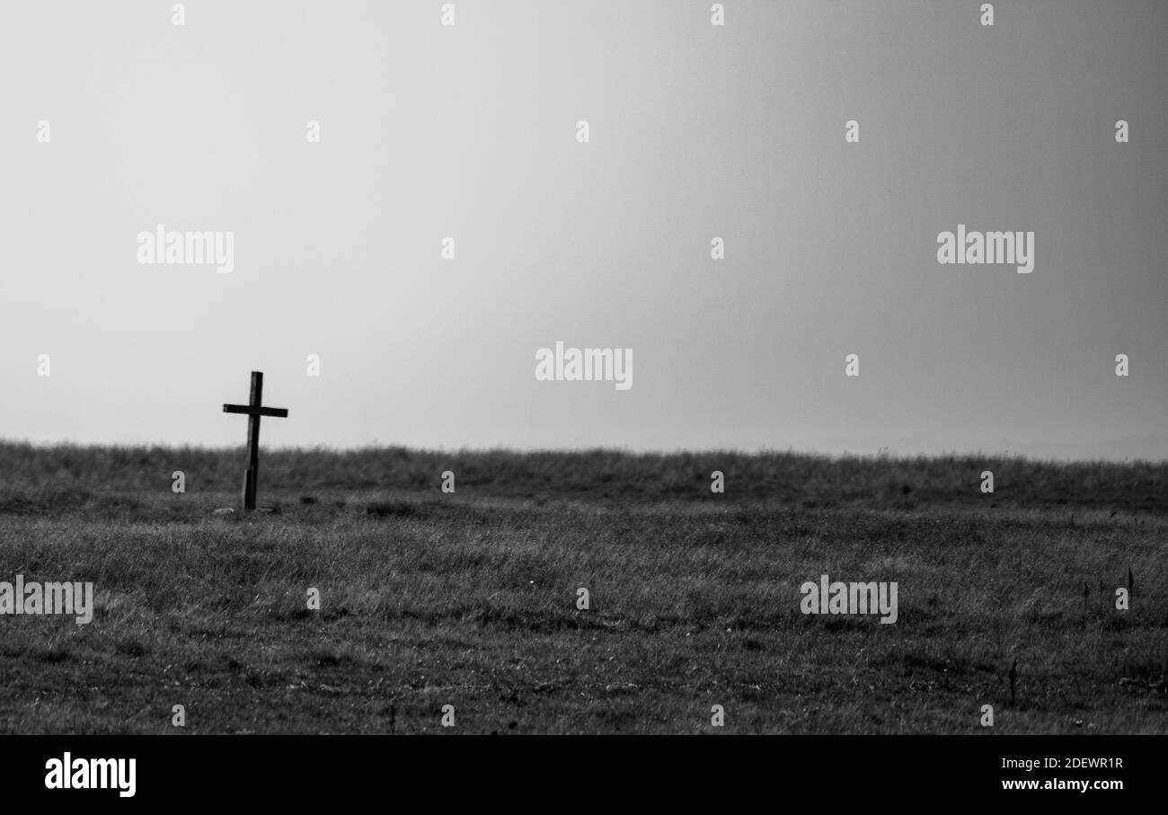 Black and white image of an old wooden Christian cross standing on a barren grass plain. . High quality photo Stock Photo