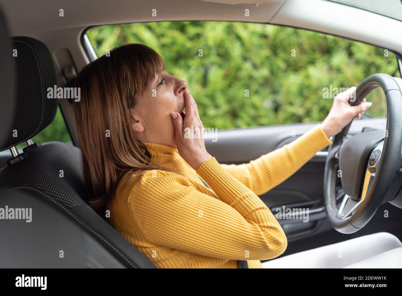Tired woman yawning behind steering wheel of car Stock Photo Alamy