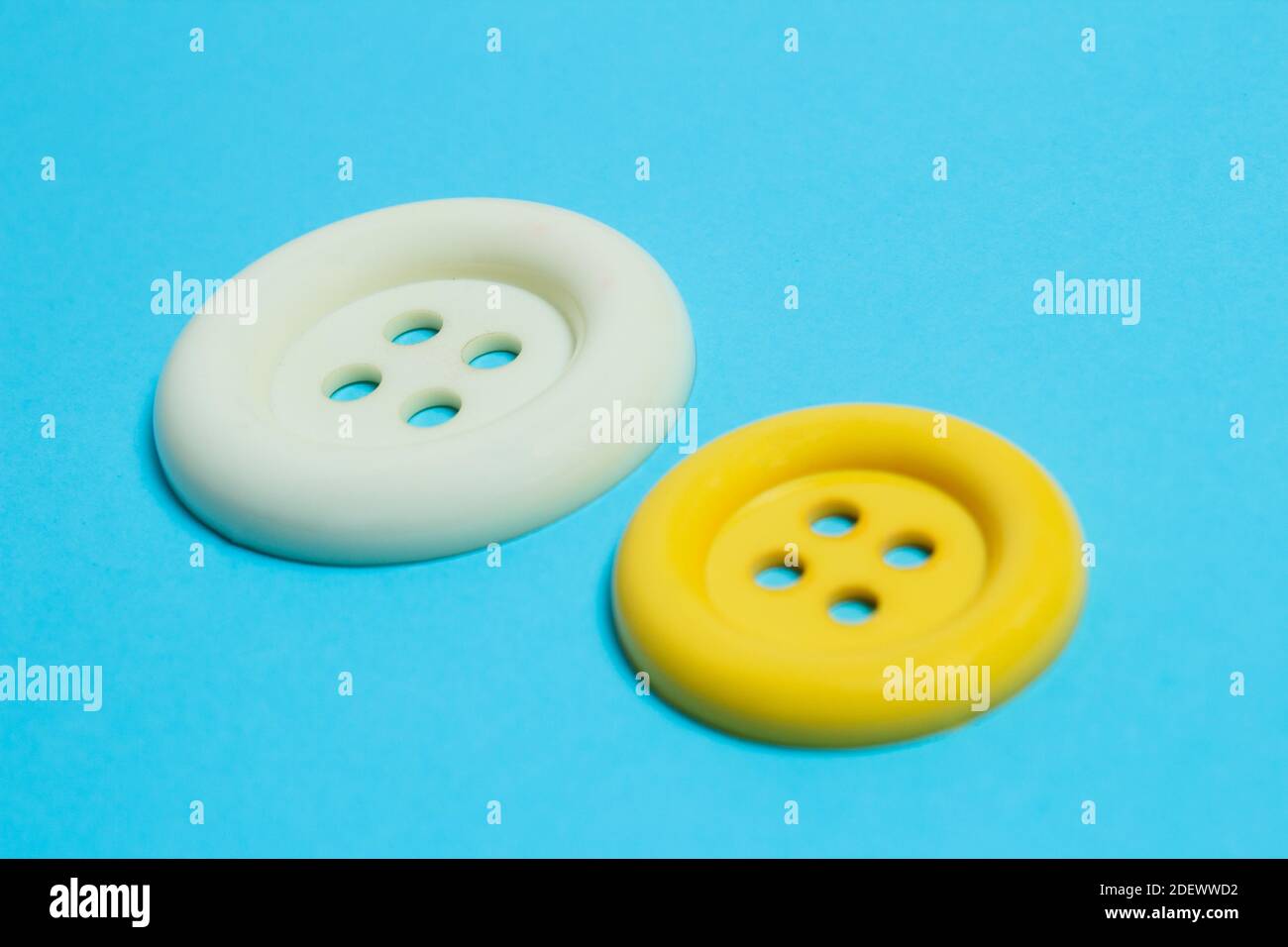 A close-up of two buttons of different sizes and colors on a light blue background. Diversity concept. Stock Photo
