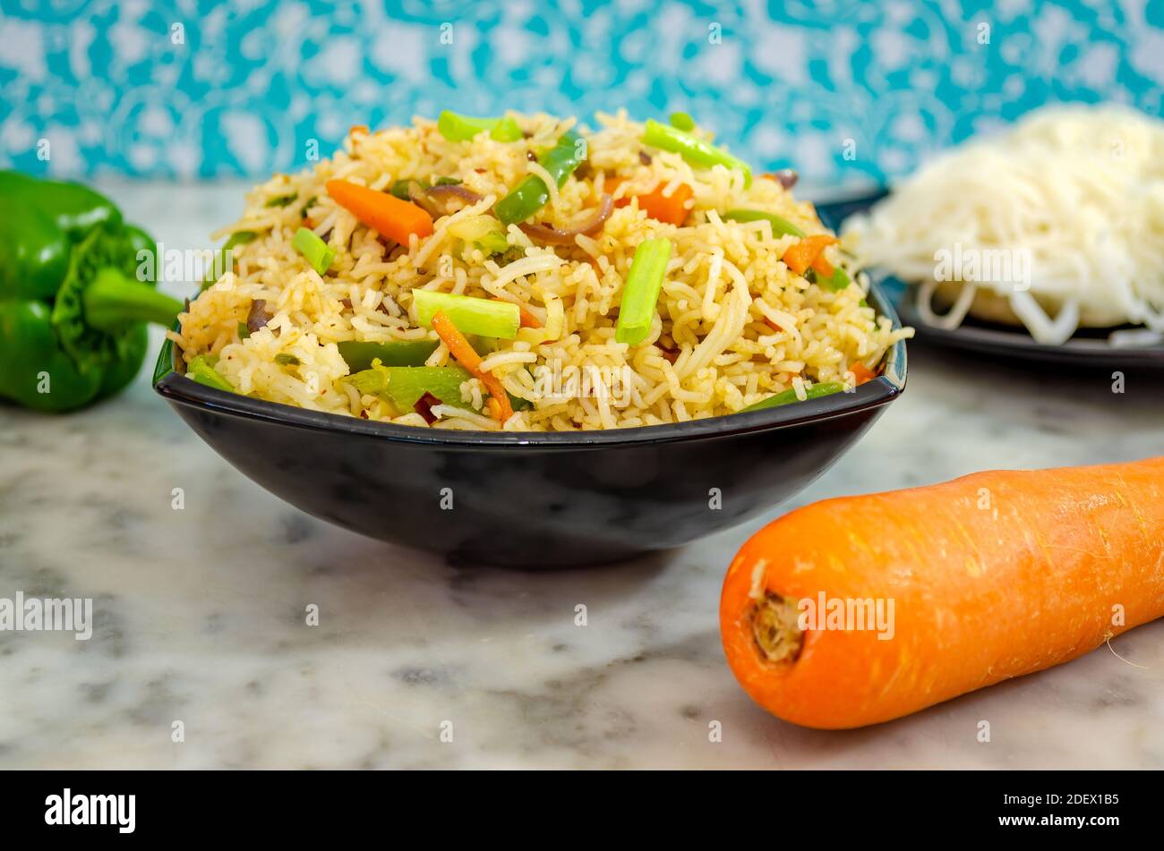 Closeup of Idiyappam Noodles (Indian Rice Noodles) in a black bowl with carrot and capsicum on the side Stock Photo