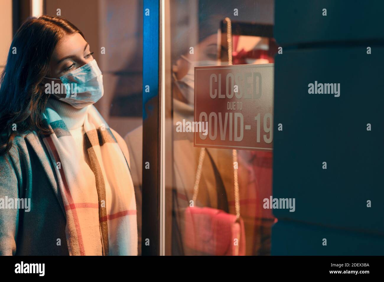 Store closed due to coronavirus covid-19 outbreak, a woman with surgical mask is reading the sign Stock Photo
