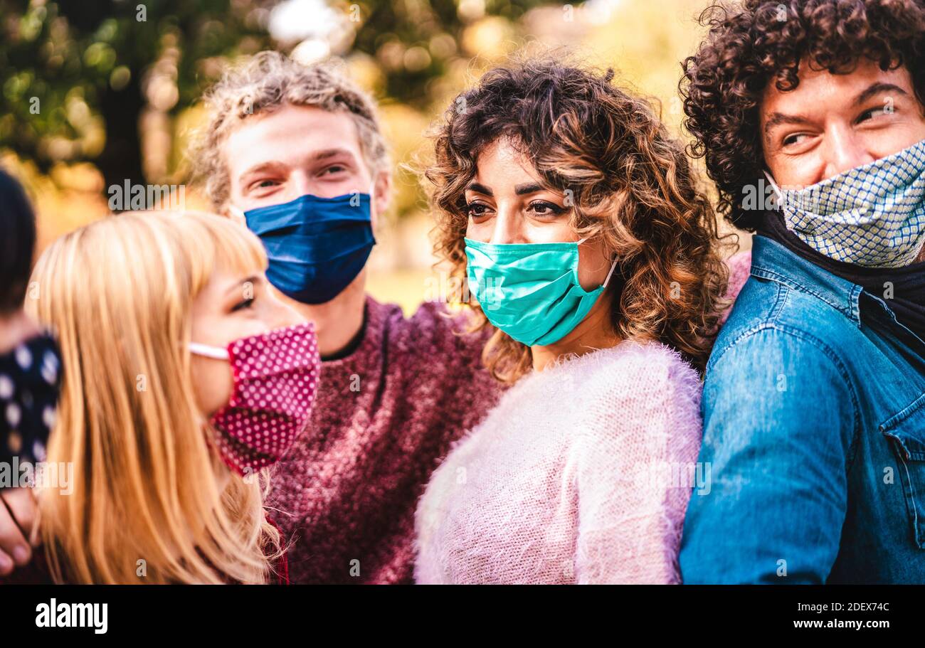 Happy multiracial friends having fun together wearing face masks - New normal friendship concept with young people sharing free time outside at park Stock Photo