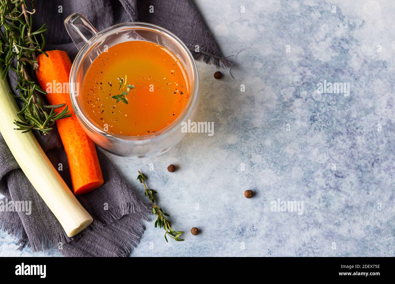 Homemade bone broth in glass mug and vegetables, blue concrete background. Collagen source for