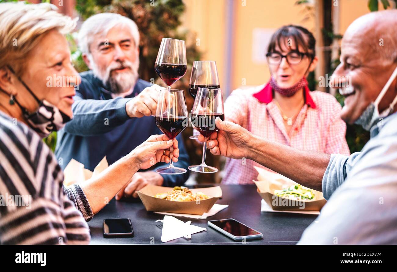 Senior people toasting wine at restaurant bar wearing opened face masks - New normal friendship concept with happy mature friends having fun together Stock Photo