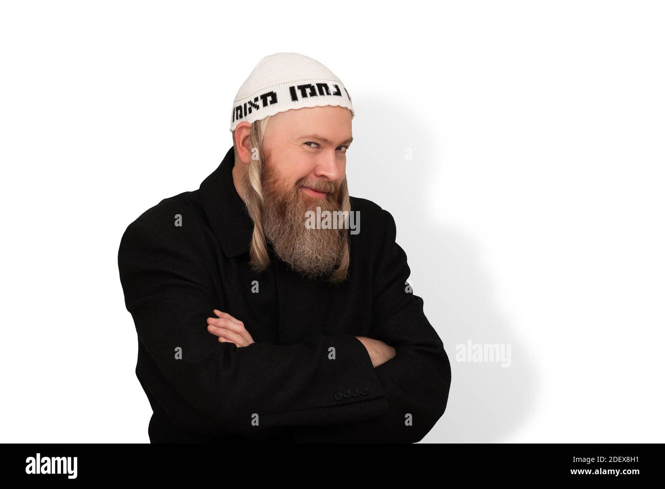 Sly bearded Jewish man smiling cunningly looking at the camera over white background. Charming jewish person with sidelocks in white kippah Stock Photo