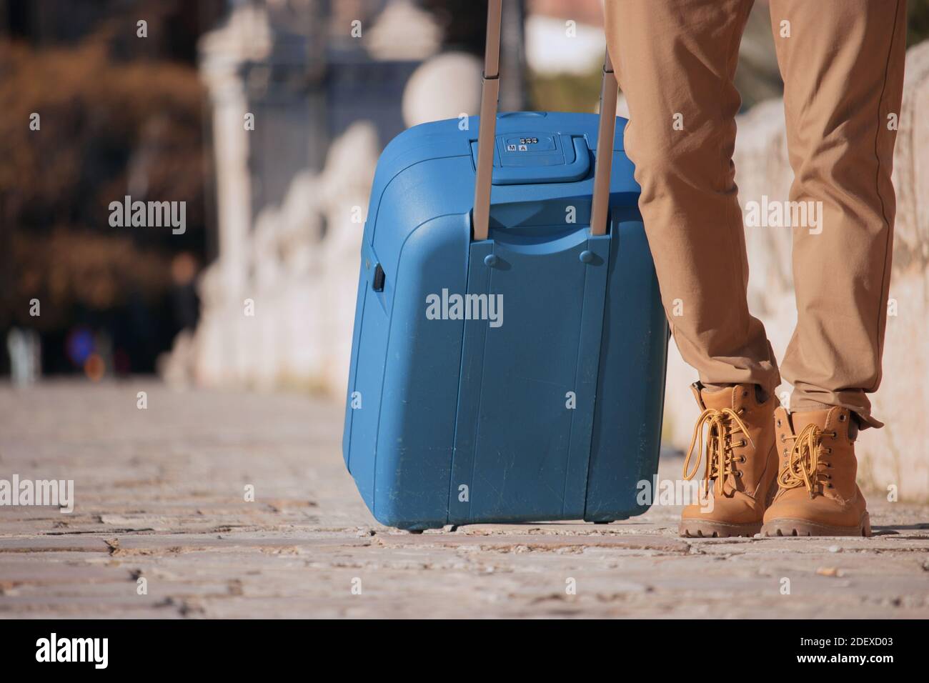 Close up unrecognizable young man travels to Spain during a pandemic with a blue suitcase while walking through downtown for bussiness work. Stock Photo