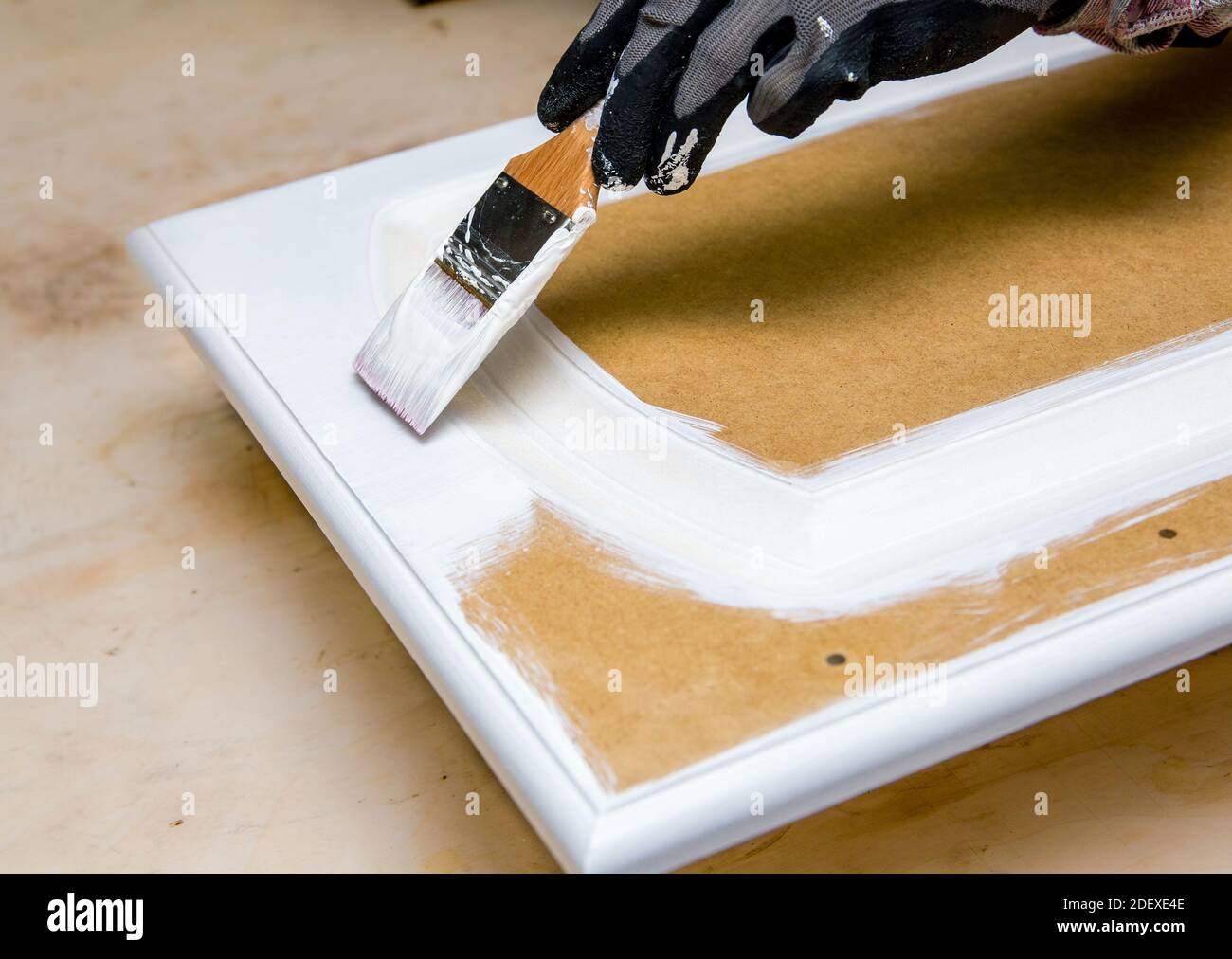 Repainting kitchen cabinet doors with white chalk paint indoors at home. Giving old kitchen new look concept. Hand holding a paint brush tool. Stock Photo