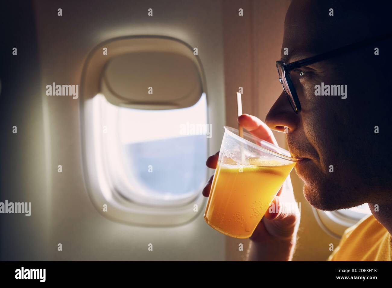 Young passenger enjoying dring during flight. Man holding cocktail against airplane window. Stock Photo