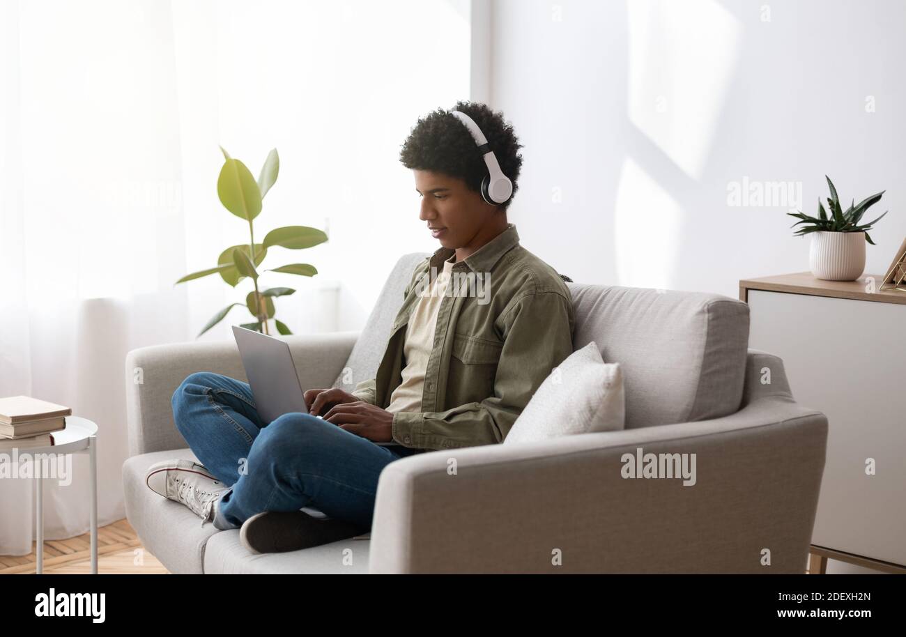 Studying from home. African American guy in headphones watching webinar, taking part in online class on laptop Stock Photo