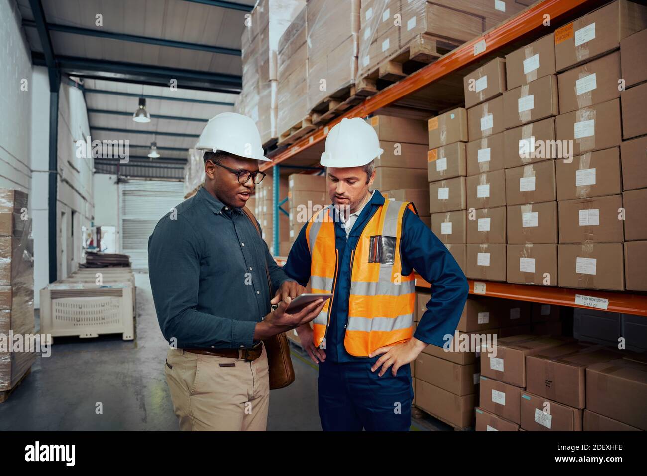 Male warehouse workers discussing about stock while using digital tablet Stock Photo