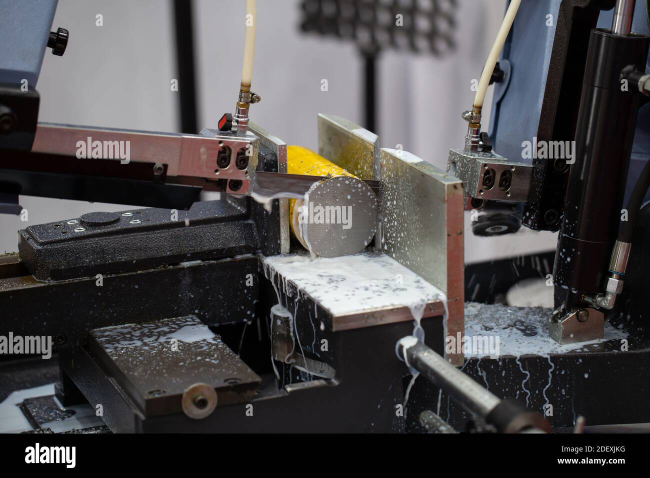 Band saw machine cutting metal rod and cooling with coolant. Industrial metalworking machinery