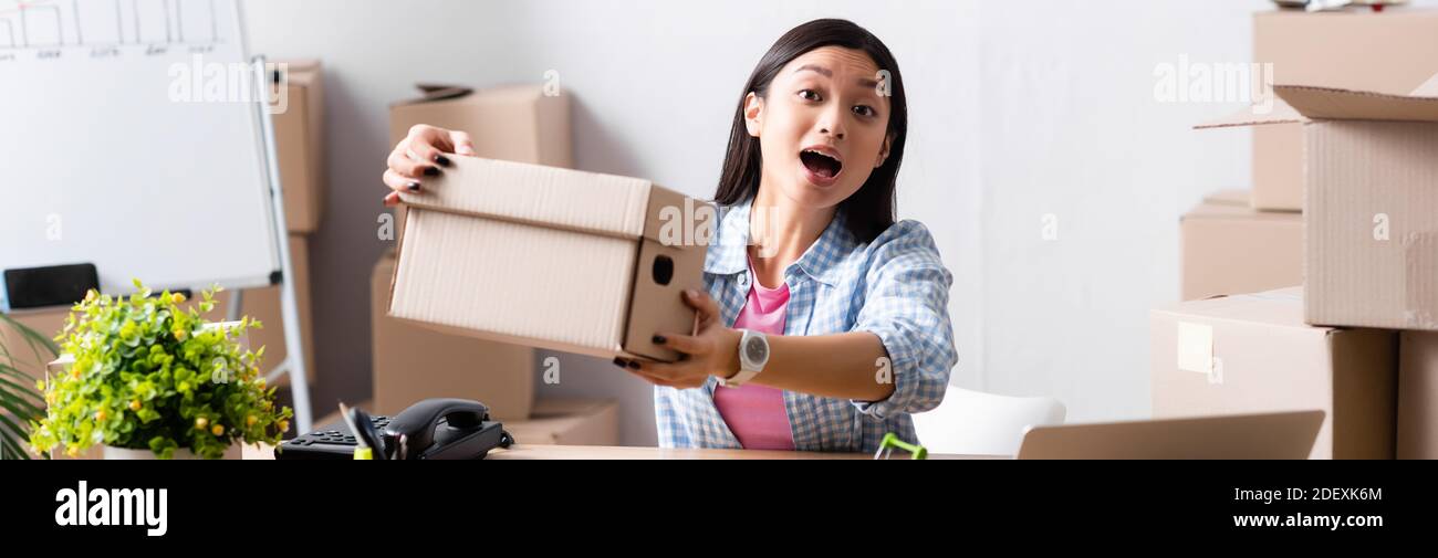 Excited asian volunteer with open mouth showing carton box in charity center, banner Stock Photo