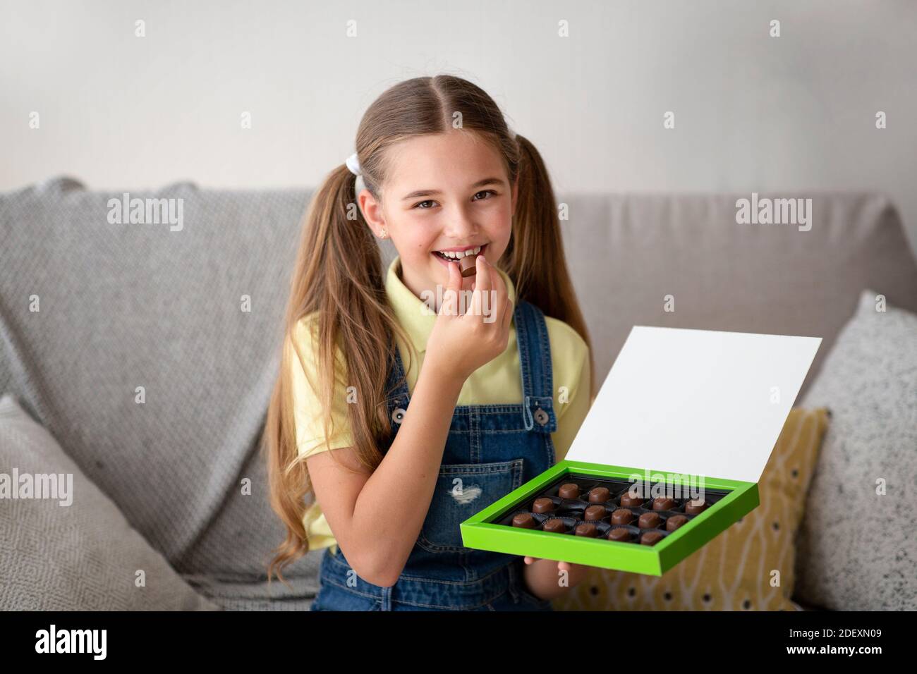 Girl eating chocolate candy sitting on a couch at home Stock Photo