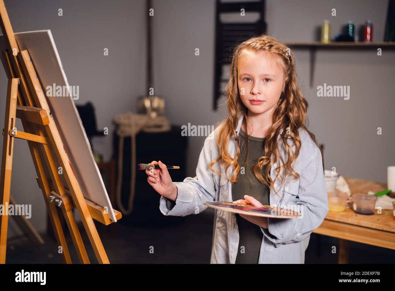 A little girl painter poses and smiles at the camera near her painting ...