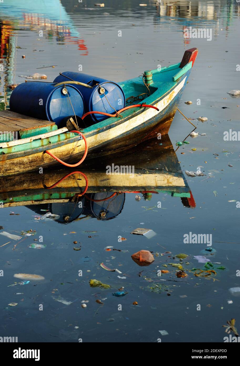 Thrown away garbage floating in polluted sea water. Boat with with gasoline barrels in Phu Quoc island, Vietnam. Stock Photo