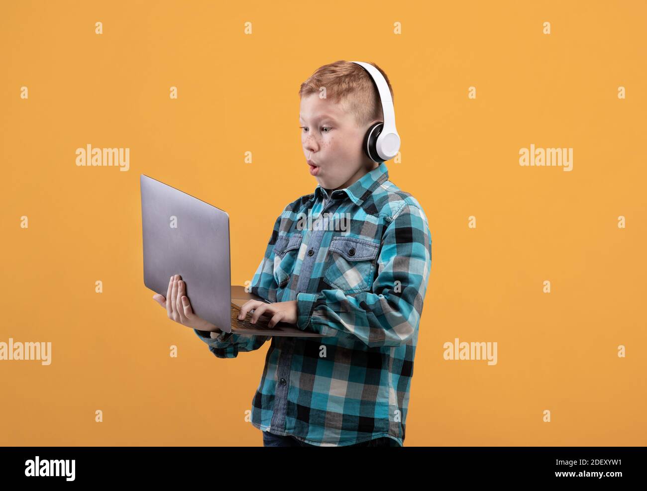 Excited redhead boy with headset playing on laptop Stock Photo
