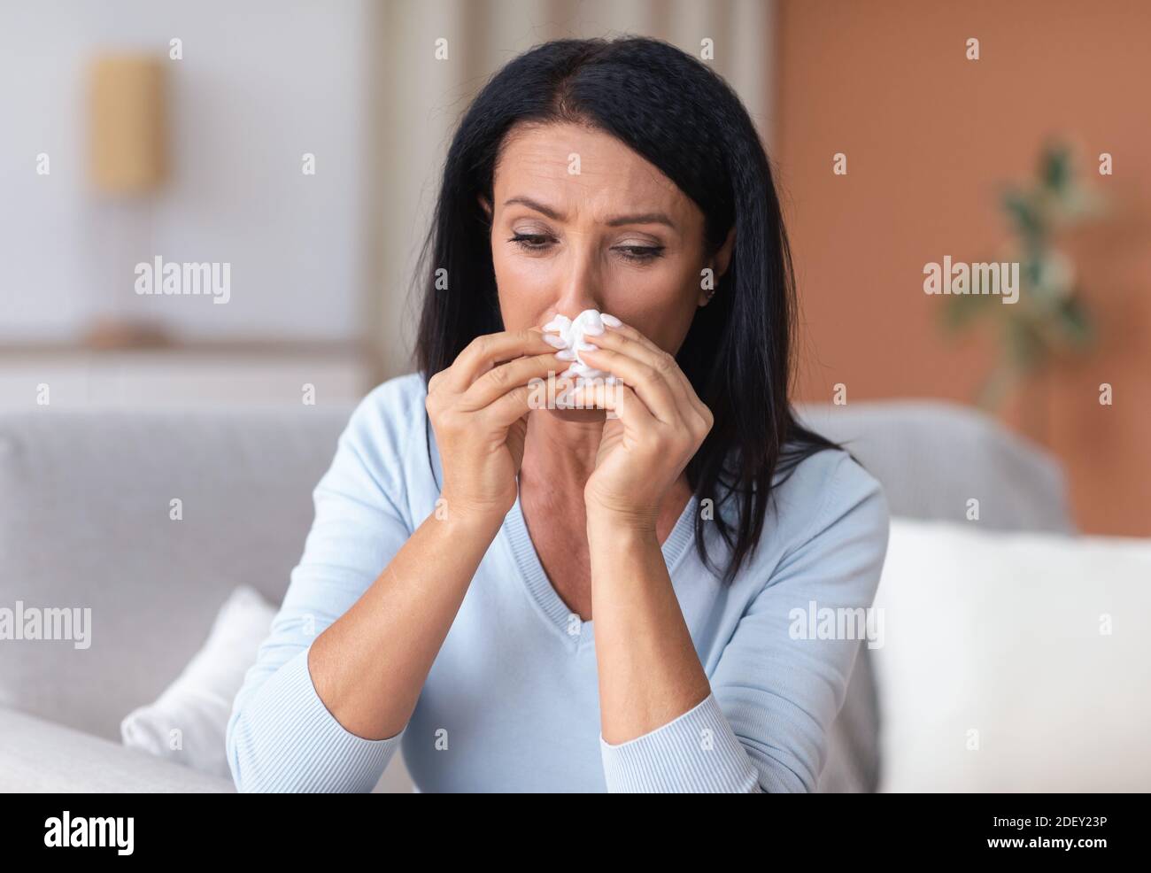 Sick mature woman sneezing and crying, holding tissue paper Stock Photo
