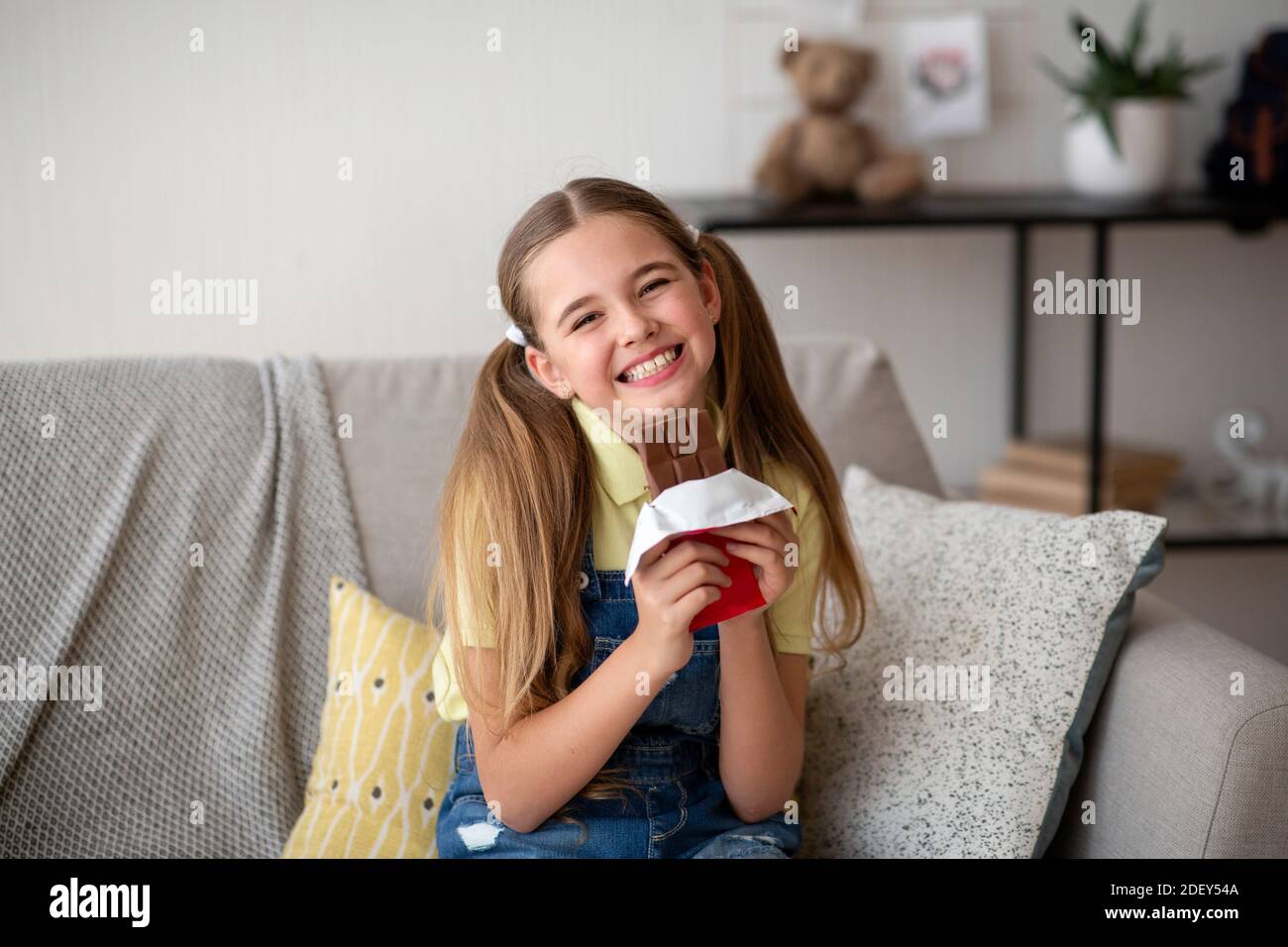 Girl eating chocolate bar sitting on a couch at home Stock Photo