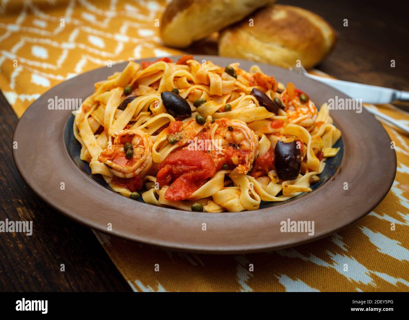 Delicious Spaghetti alla puttanesca with jumbo shrimp and fresh italian bread Stock Photo