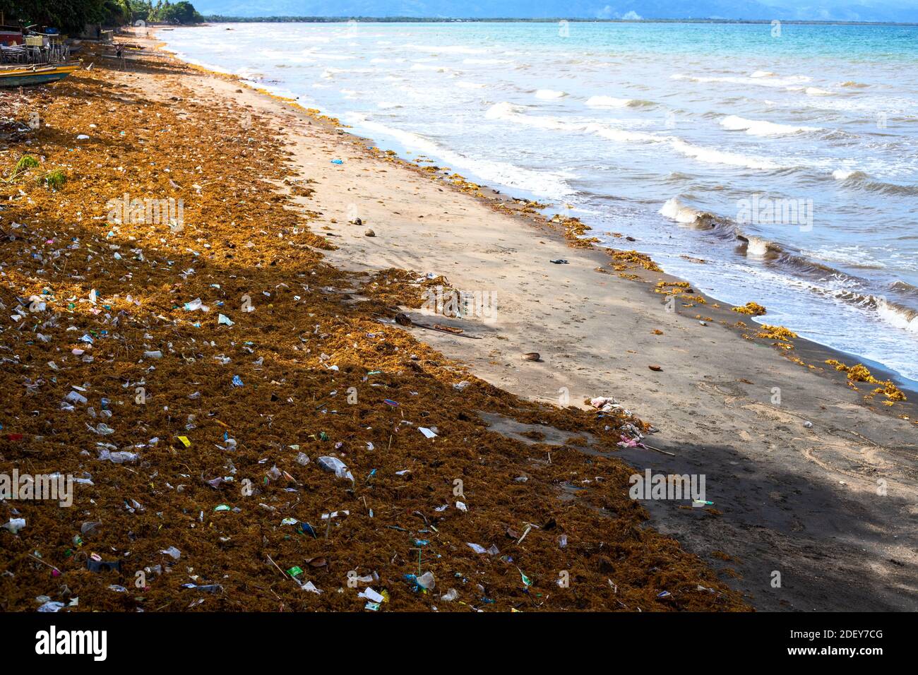 Sea water with waves, seaweed and garbage. Aquatic trash on tropical beach. Plastic pollution in ocean. Environmental problem of human impact on natur Stock Photo