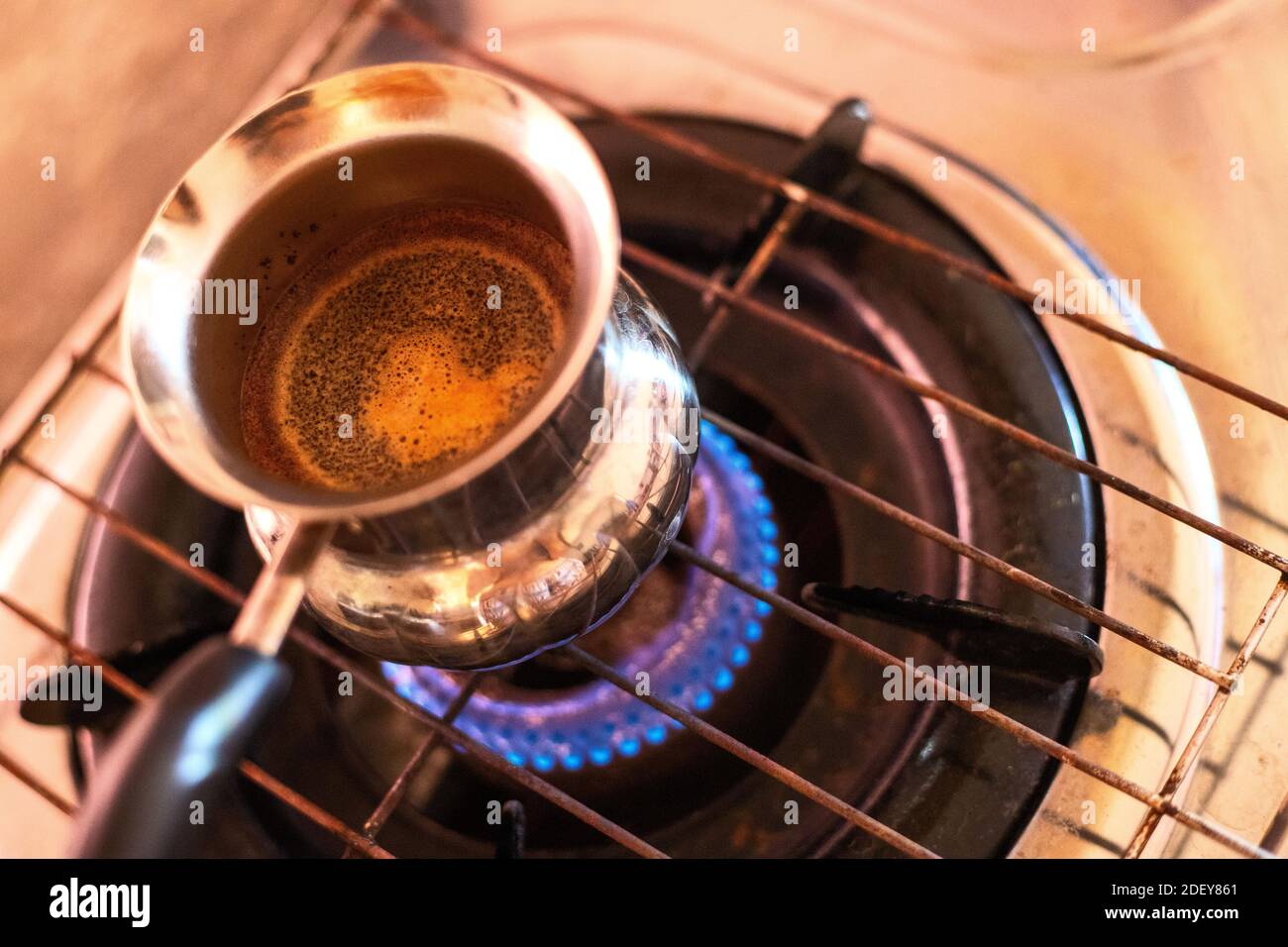 Brown coffee in turk on gasoline stove. Turkish coffee brewing in cezve. Boiling black coffee on fire. Morning breakfast routine. Refreshment drink re Stock Photo