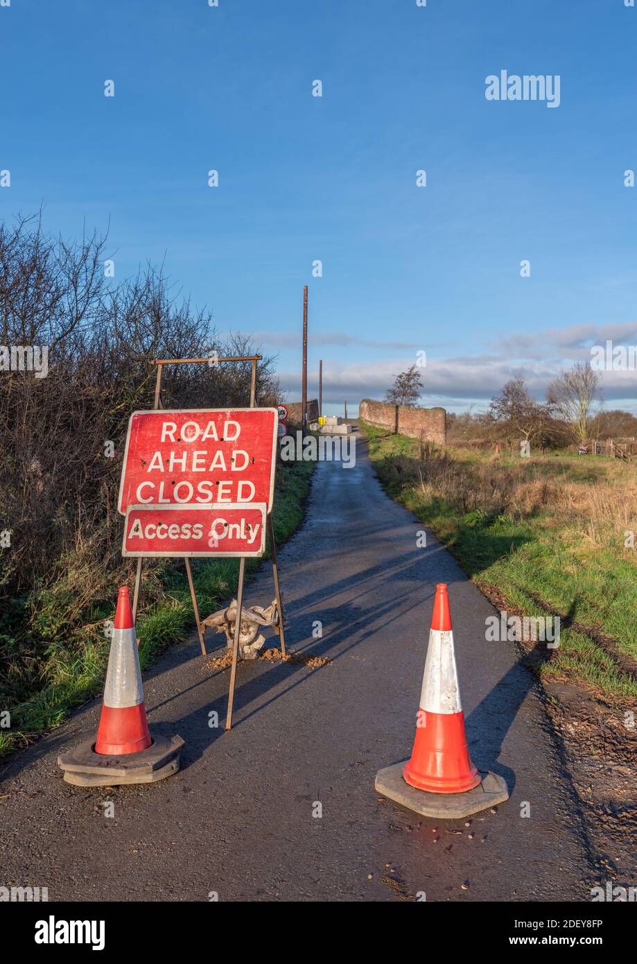 Road ahead closed sign and 2 red and white traffic cones on approach to a closed bridge. Stock Photo