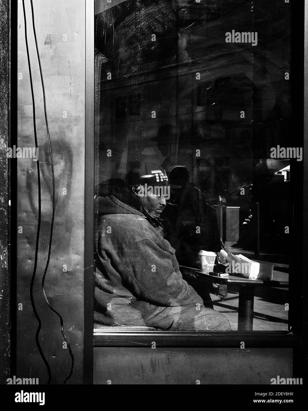 Brooklyn, New York, NY, USA - November 30, 2019. Old man sitting in front of a window in Dunkin' Donuts bakery, Brooklyn, New York City. Stock Photo