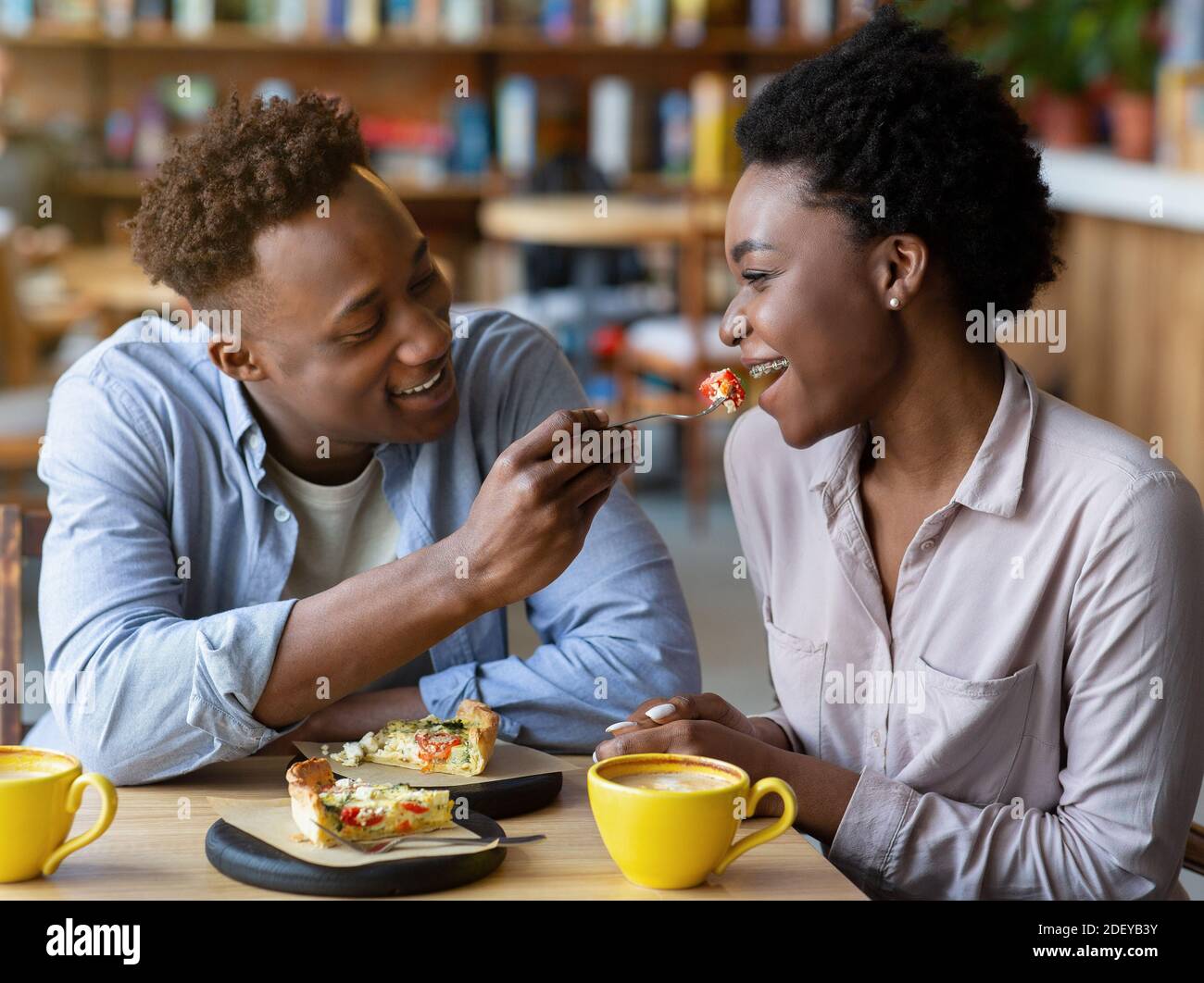 Millennial black guy feeding tasty quiche cake to his girlfriend at cozy  urban cafe Stock Photo - Alamy