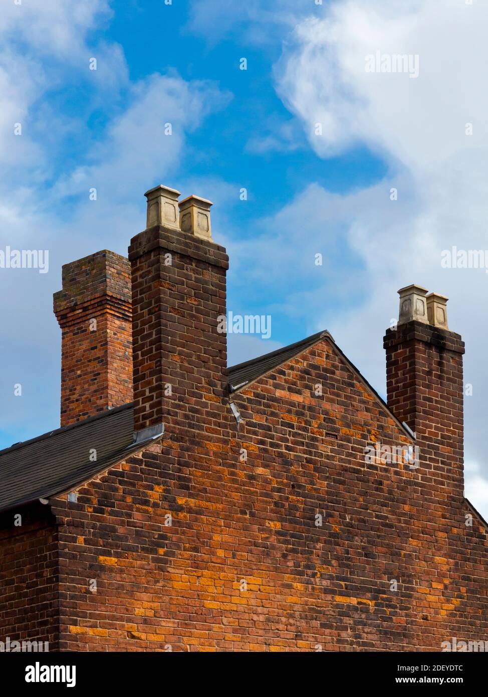 End wall of a red brick house with chimney pots and blue sky with clouds above. Stock Photo